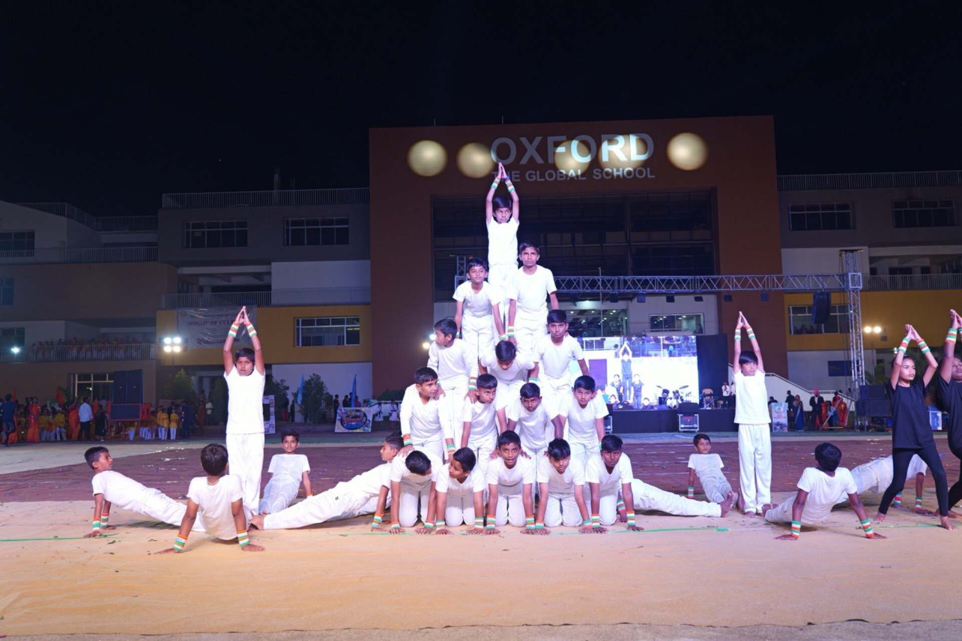 Students forming a gymnastic pyramid in front of the school building at night