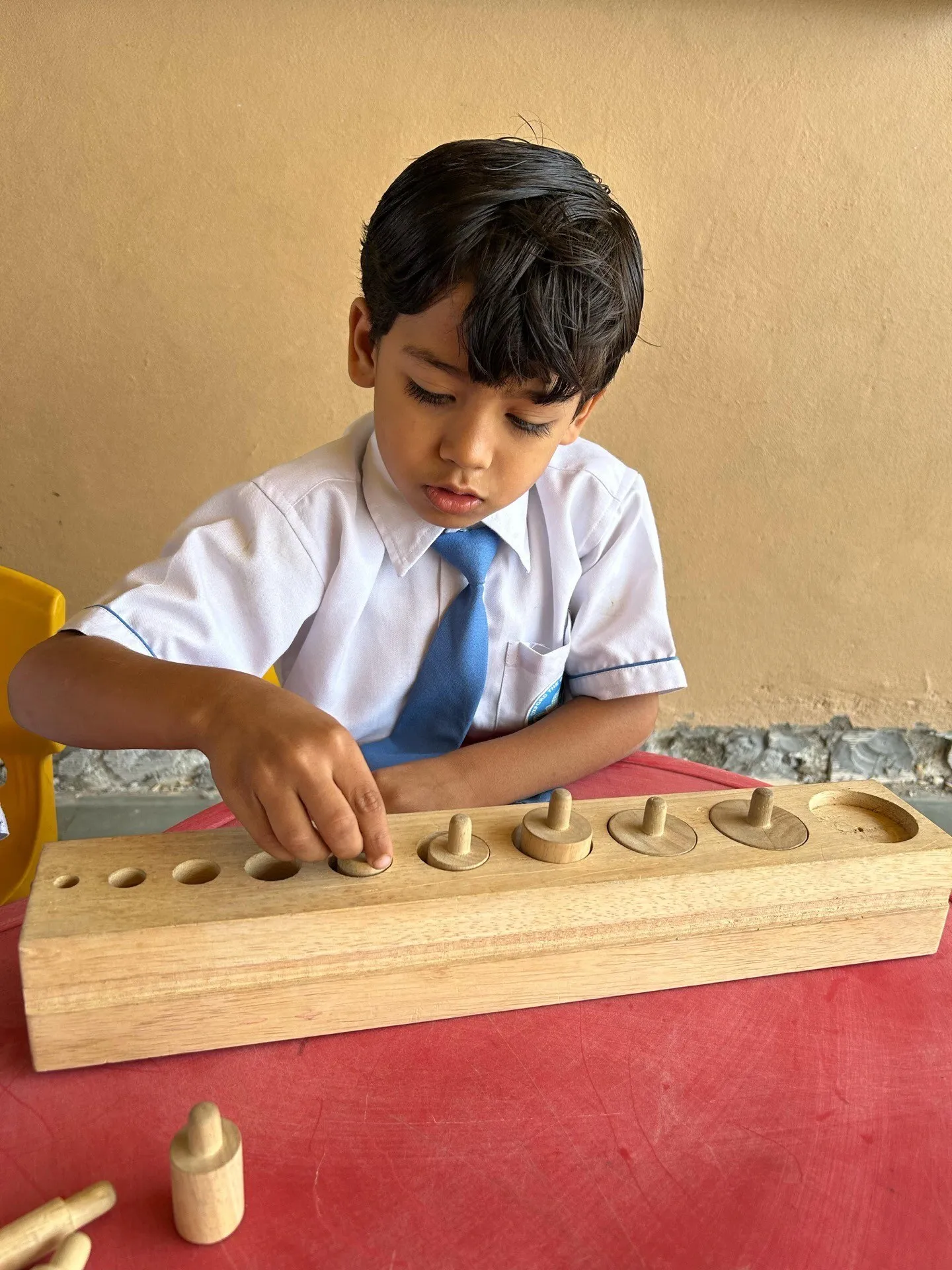A young boy carefully placing cylinders into a wooden learning block