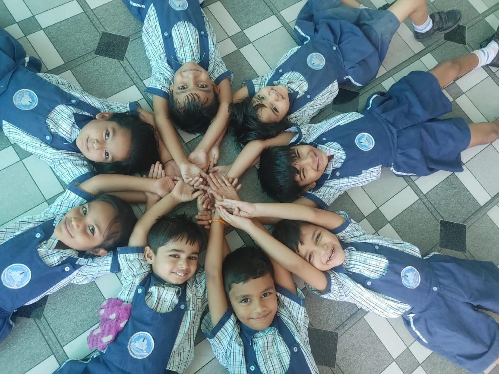 Pre-primary children lying in a circle with their hands joined at the centre